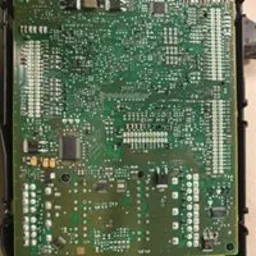 Zielona płytka drukowana z licznymi elementami elektronicznymi i złączami, umieszczona w czarnej ramce. Widoczne ślady pasty lutowniczej i drobne zabrudzenia.