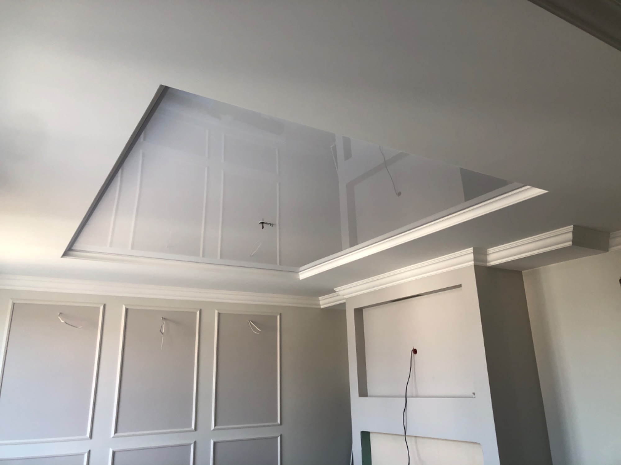 Wnętrze w trakcie wykańczania: ściany z dekoracyjnymi panelami i listwami, sufit podwieszany z wnęką, widoczne kable wystające ze ścian.
