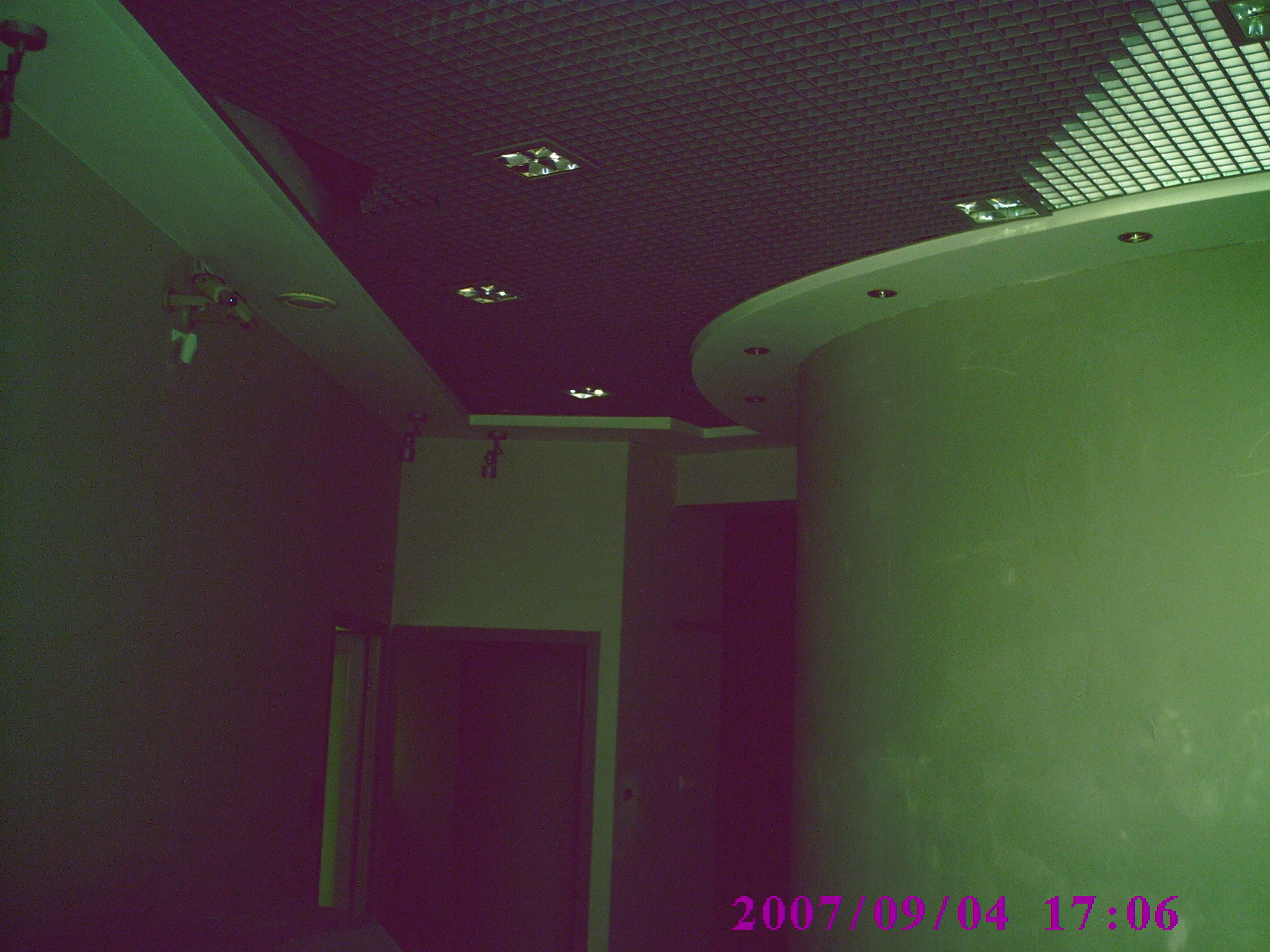 Wnętrze biurowe z podwieszanym sufitem kasetonowym, oświetleniem punktowym i zaokrąglonymi elementami architektonicznymi, sfotografowane z perspektywy podłogi.