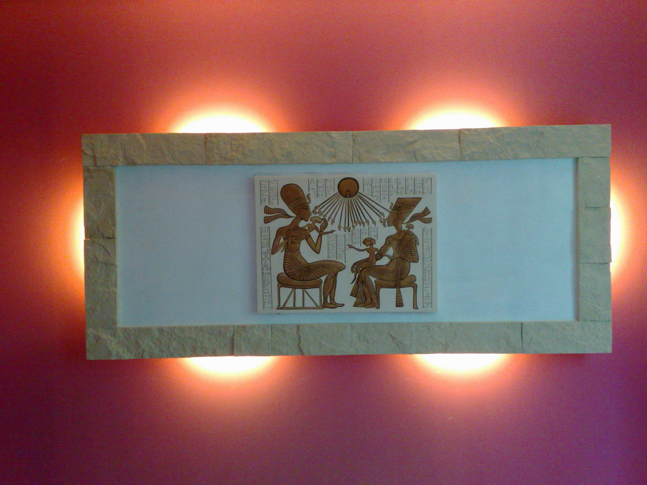 Panel dekoracyjny z motywem egipskim, podświetlony dwoma lampami, na różowej ścianie z efektem ombre.