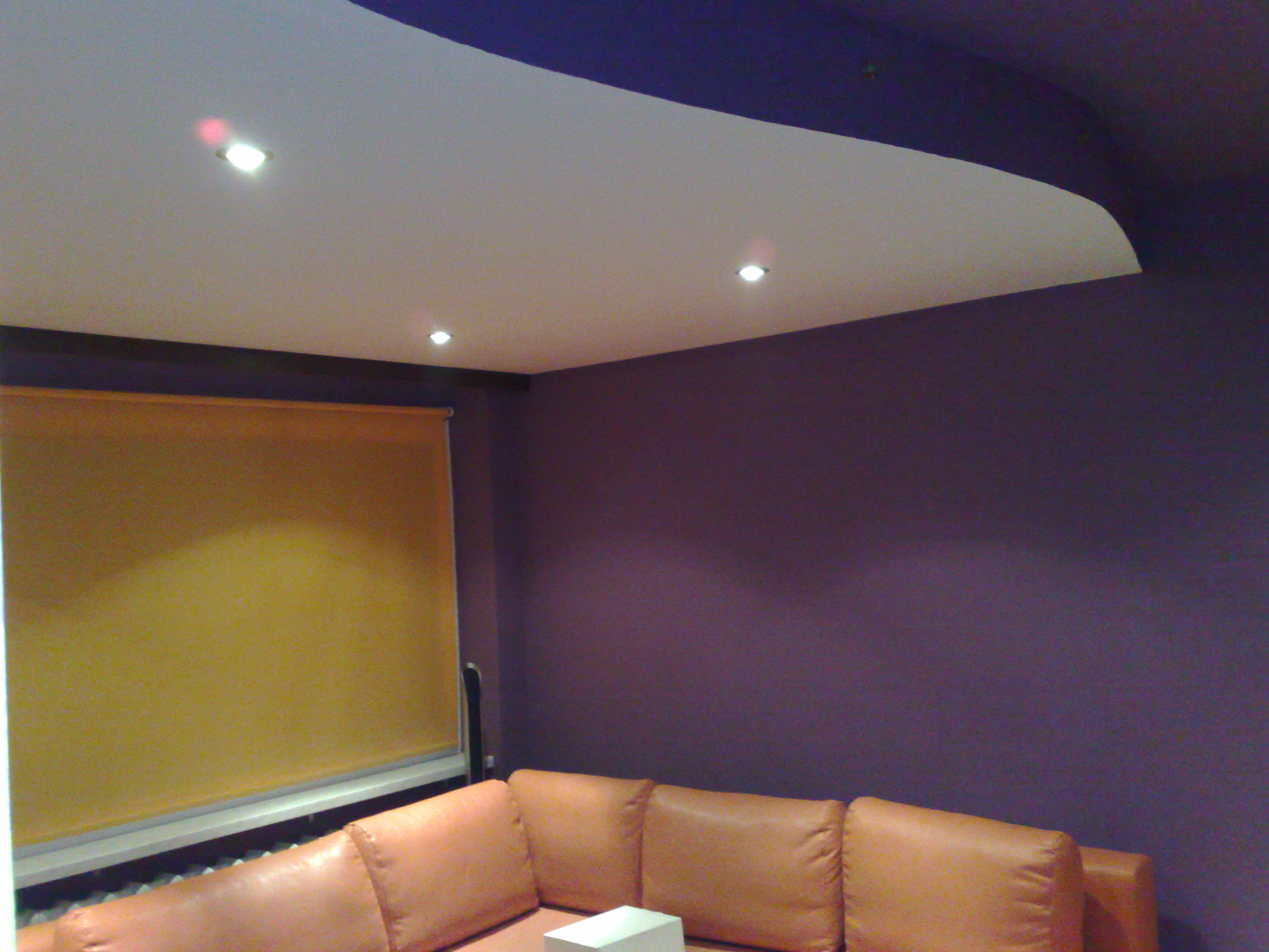 Fioletowa ściana w pokoju z pomarańczową roletą i narożnikiem, podwieszany biały sufit z oświetleniem punktowym.