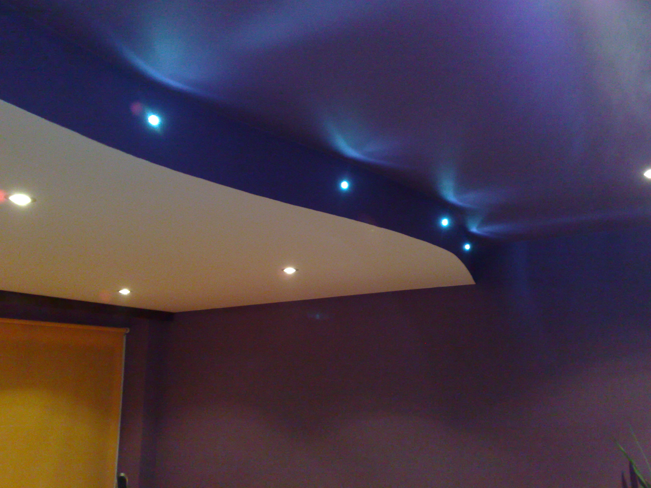 Fioletowy sufit z podwieszaną białą konstrukcją i punktowym oświetleniem LED, widoczna roleta okienna w kolorze żółtym.