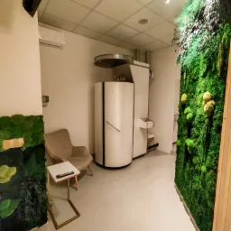 Wnętrze gabinetu z kriokomorą, ścianą z mchu i minimalistycznym wystrojem, oświetlone światłem punktowym.