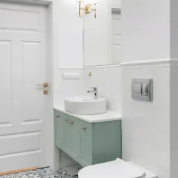 Nowoczesna łazienka w bieli z akcentami pastelowej zieleni: szafka pod umywalkę, wzorzysta podłoga i wisząca toaleta.