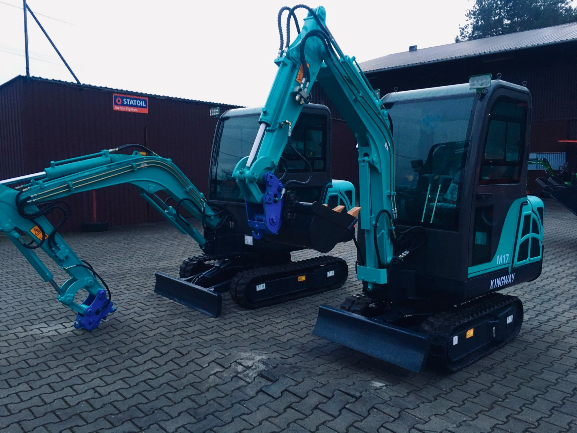 Dwie mini koparki Kingway M17 w Łodzi, ustawione na brukowanym placu przed budynkiem Statoil, z widocznymi detalami hydrauliki i osprzętu.