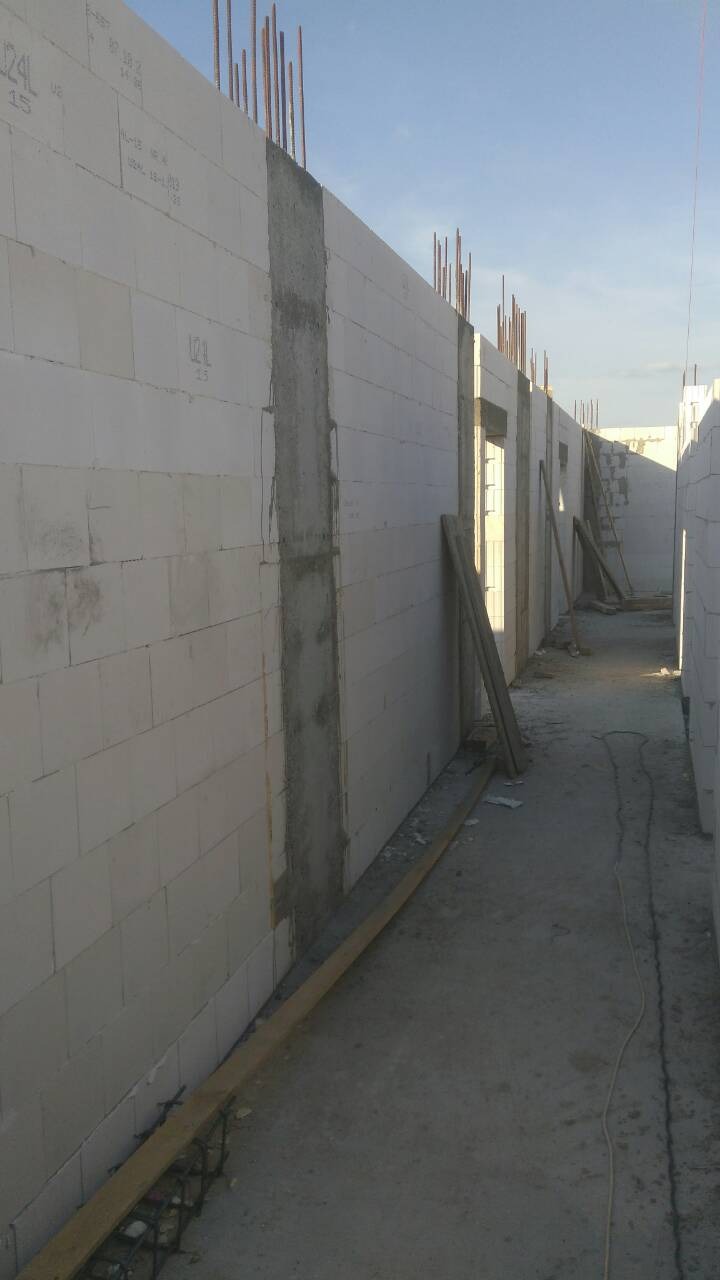 Wznoszenie ścian budynku z bloczków betonowych z widocznymi zbrojeniami pionowymi i częściowo wylane słupy betonowe.