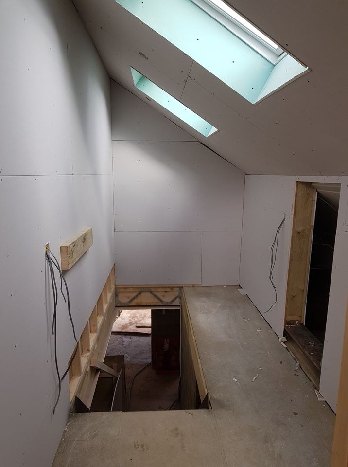 Poddasze w trakcie adaptacji: ściany obłożone płytami gipsowo-kartonowymi, widoczne okna dachowe, przygotowane otwory na schody i instalację elektryczną.