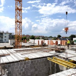 Kascad Sp. z o.o. - Budowa budynku wielorodzinnego w Opolu: widok z góry na zbrojenie stropu, częściowo wymurowane ściany z betonu komórkowego, dźwig podający beton i pracujących robotników w kamizelkach odblaskowych.