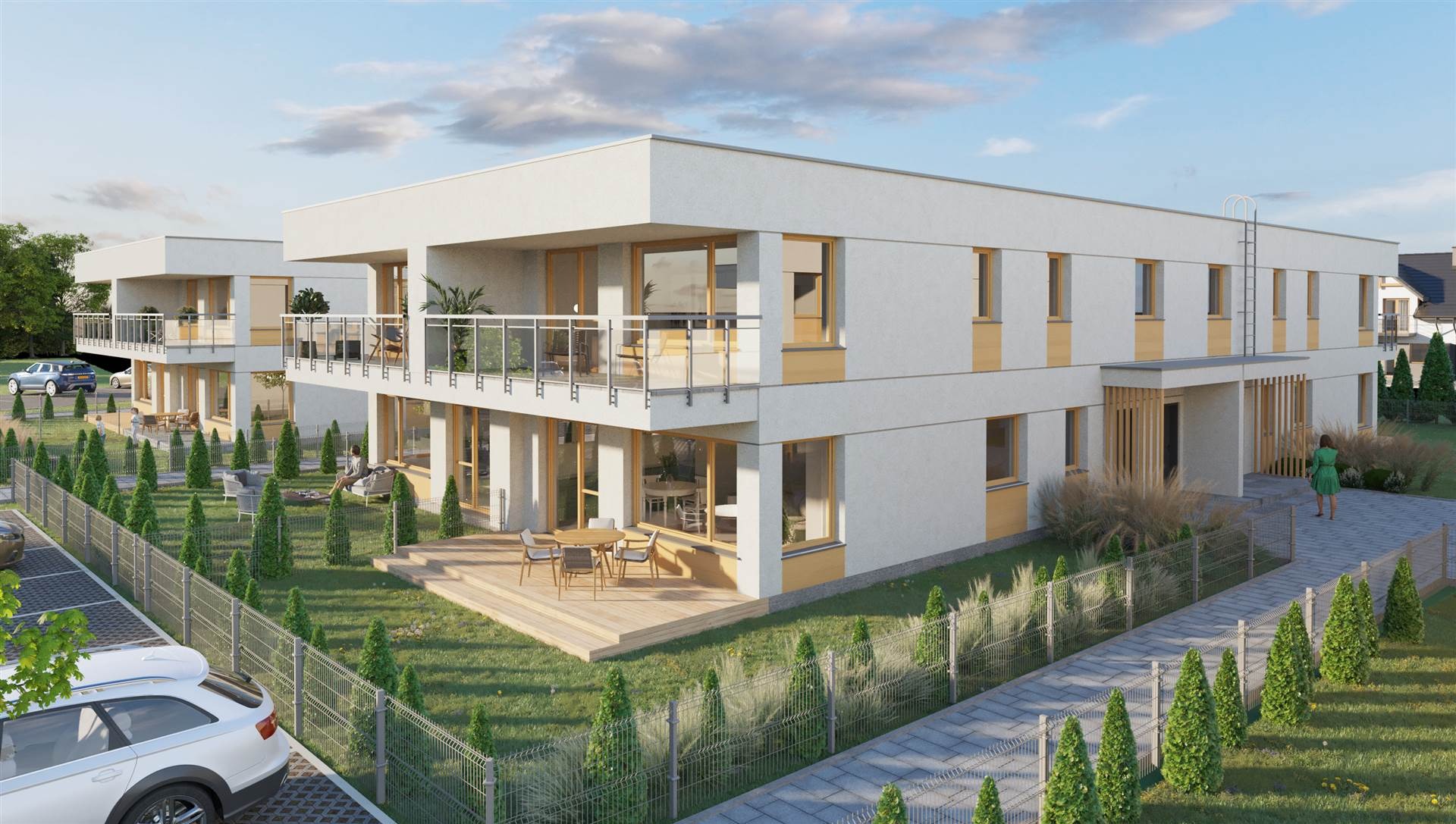 Wizualizacja osiedla domów wielorodzinnych z płaskim dachem i drewnianymi tarasami, otoczonych zielenią i ogrodzeniem z siatki. Na pierwszym planie zaparkowany samochód.