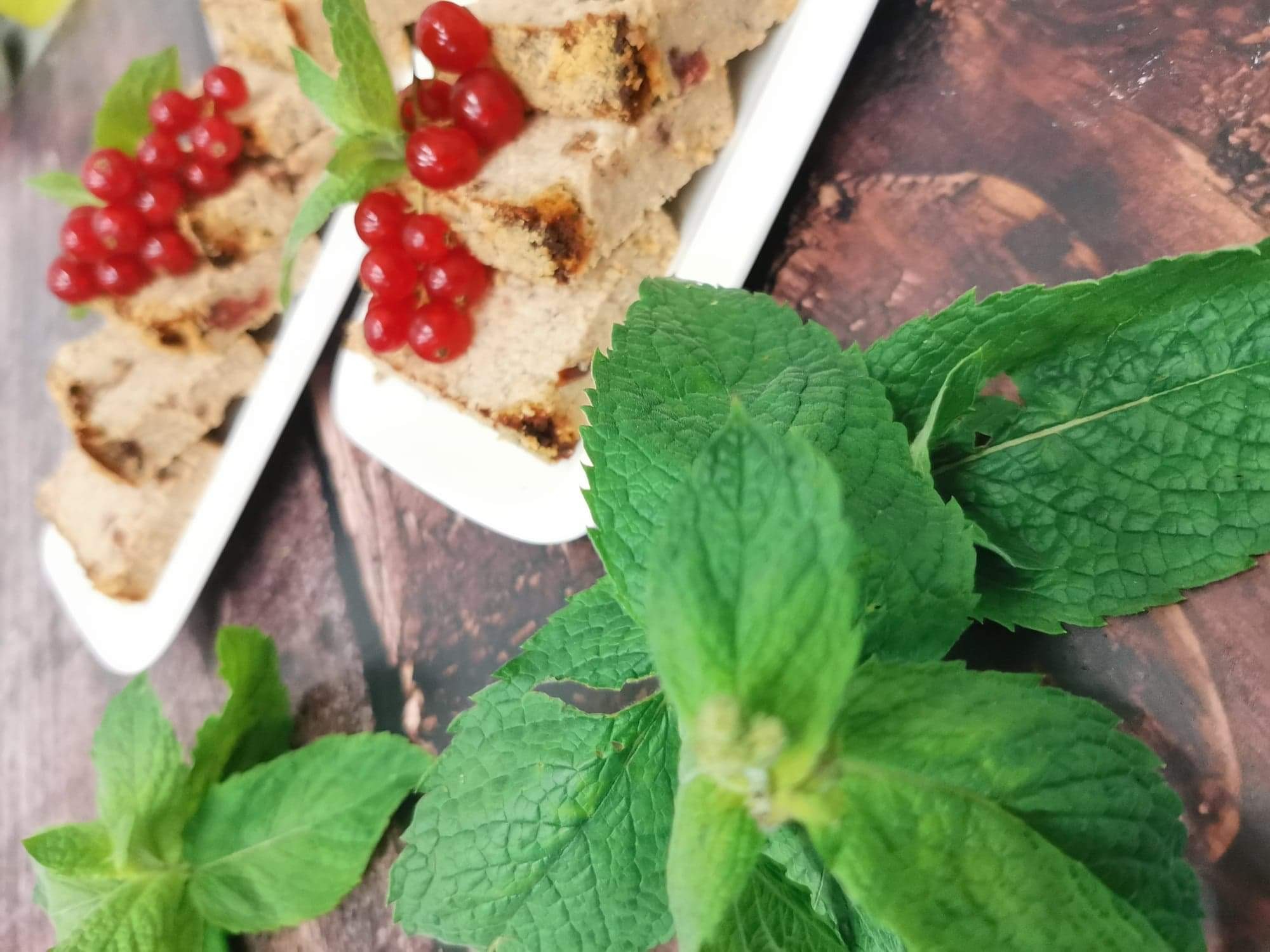 Krojony pasztet na białym talerzu, udekorowany świeżą czerwoną porzeczką i gałązkami mięty, na drewnianym tle.