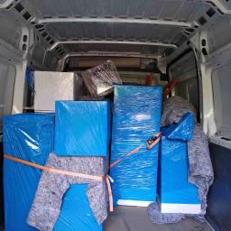 MoveHERO - Wnętrze furgonetki wypełnionej zabezpieczonymi paczkami i meblami do przeprowadzki we Wrocławiu, owiniętymi w niebieską folię i szare koce, zabezpieczone pomarańczowymi pasami.