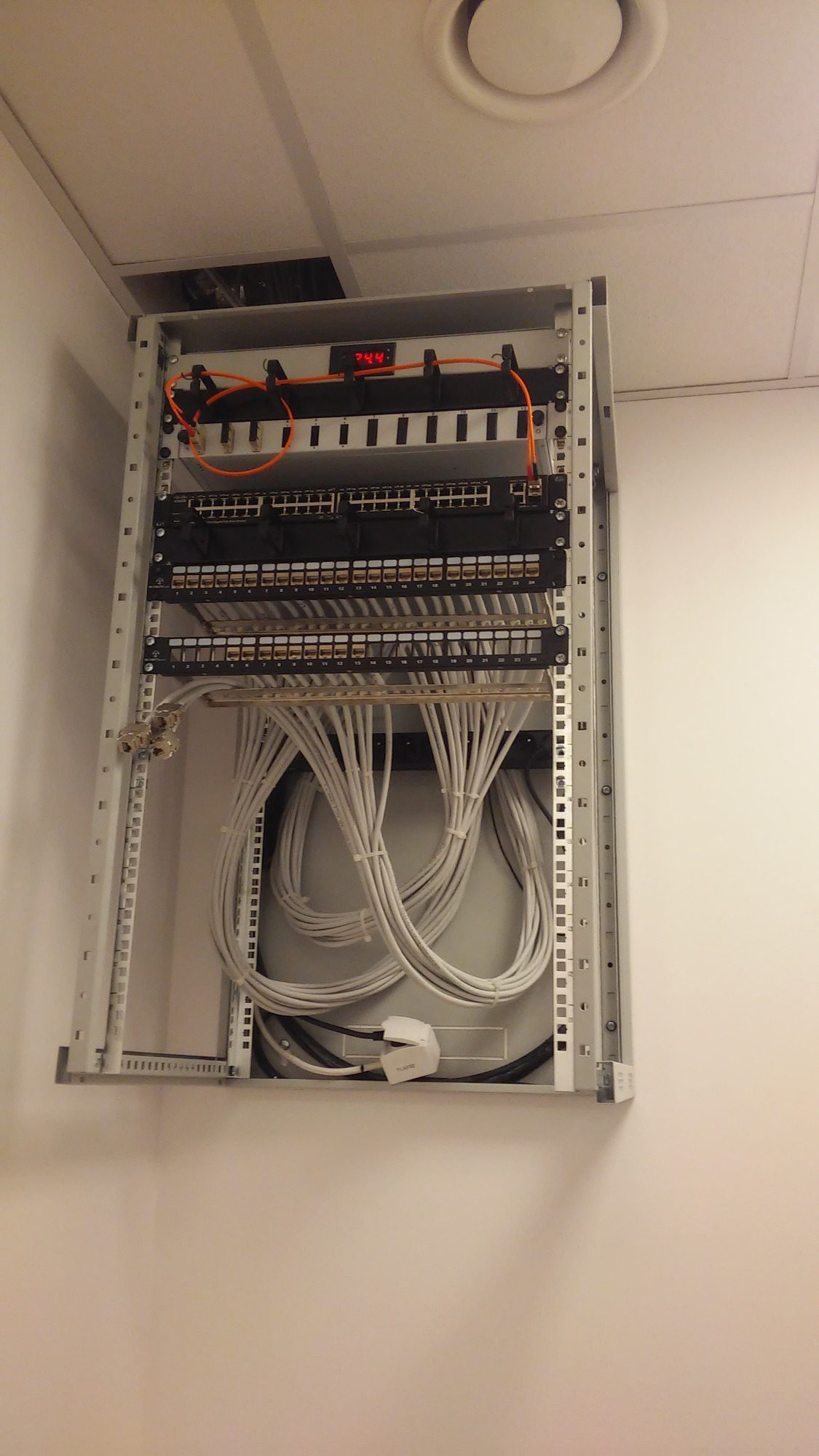 Szafa rack z okablowaniem sieciowym w biurze, widoczne patch panele, switche i uporządkowane kable kategorii 5e/6, zasilacz awaryjny w dolnej części szafy.