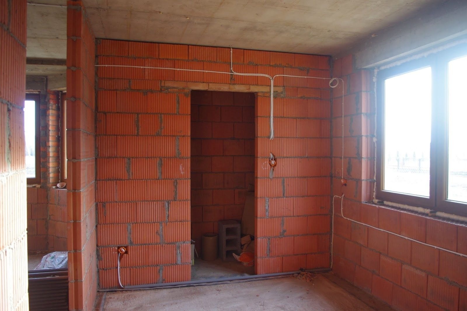 Surowy stan wnętrza z czerwonej cegły w Słupsku, widoczne poprowadzone przewody elektryczne, puszki pod gniazdka i otwór drzwiowy.