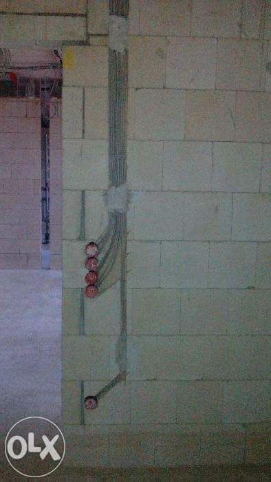 Ściana z betonu komórkowego w trakcie montażu przewodów elektrycznych; widoczne otwory pod gniazdka i puszki instalacyjne.