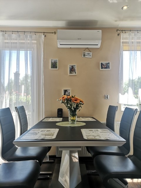 Wnętrze jadalni z zamontowanym klimatyzatorem ściennym nad stołem z bukietem pomarańczowych kwiatów.