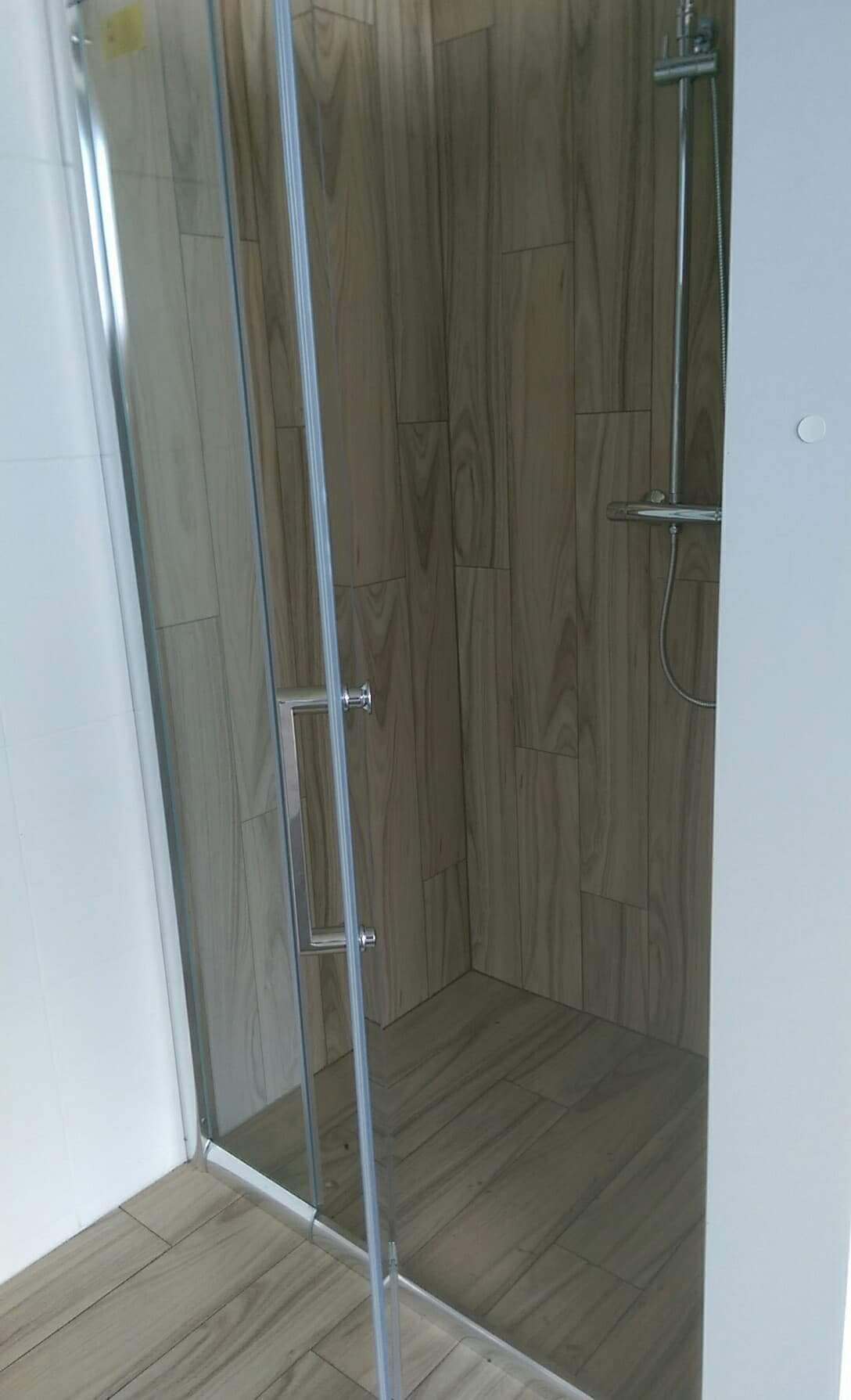 Kabina prysznicowa z drzwiami ze szkła hartowanego, wykończona płytkami imitującymi drewno, zamontowana w łazience w Kaliszu.
