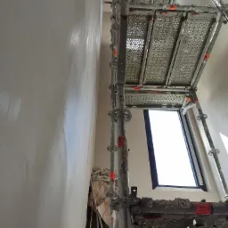 Świeżo otynkowana ściana w trakcie rewitalizacji kamienicy, widoczny fragment instalacji elektrycznej i rusztowanie.