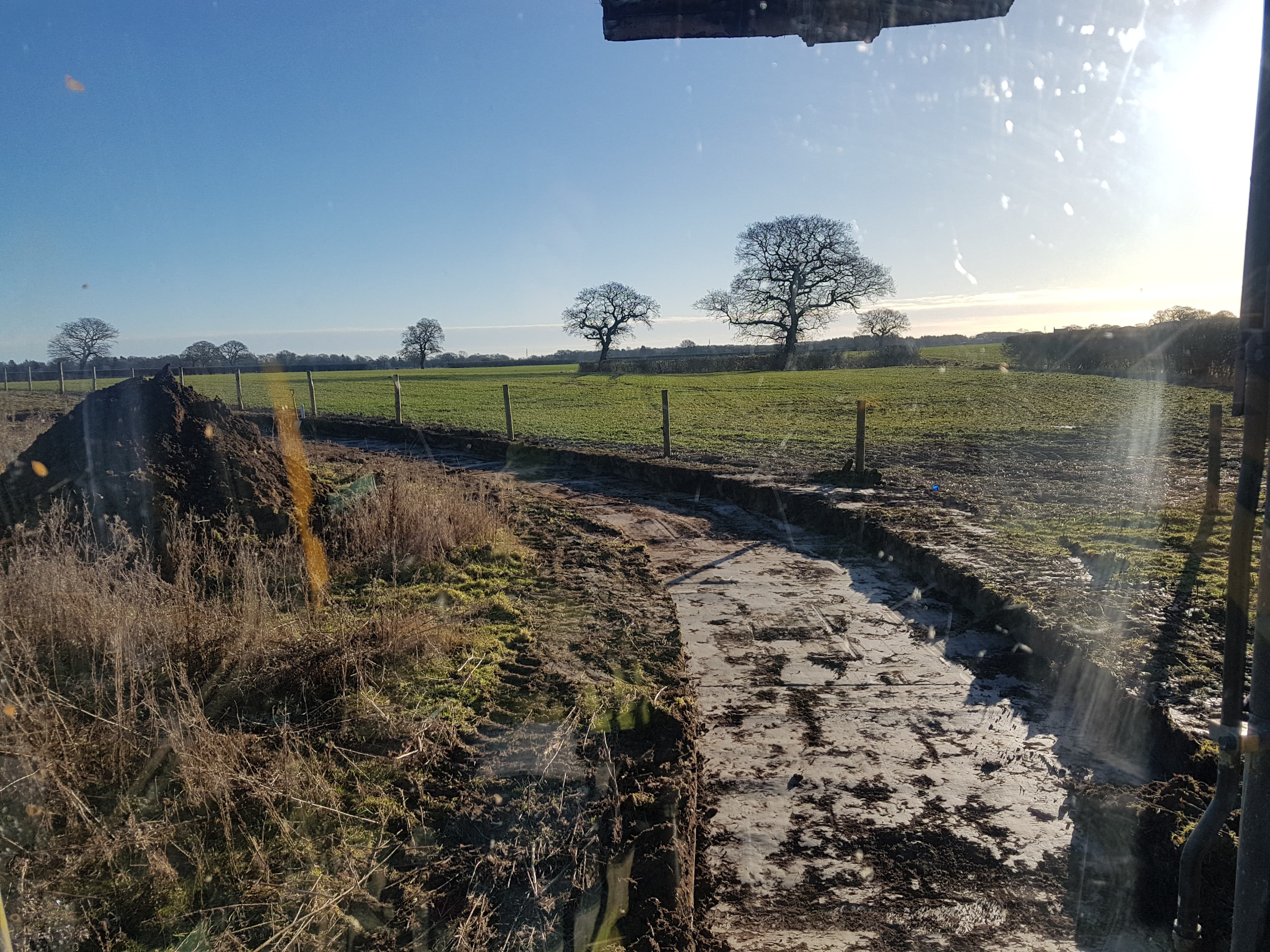 Świeżo wykopany rów w polu, widok z kabiny maszyny, w tle drzewa i błękitne niebo.
