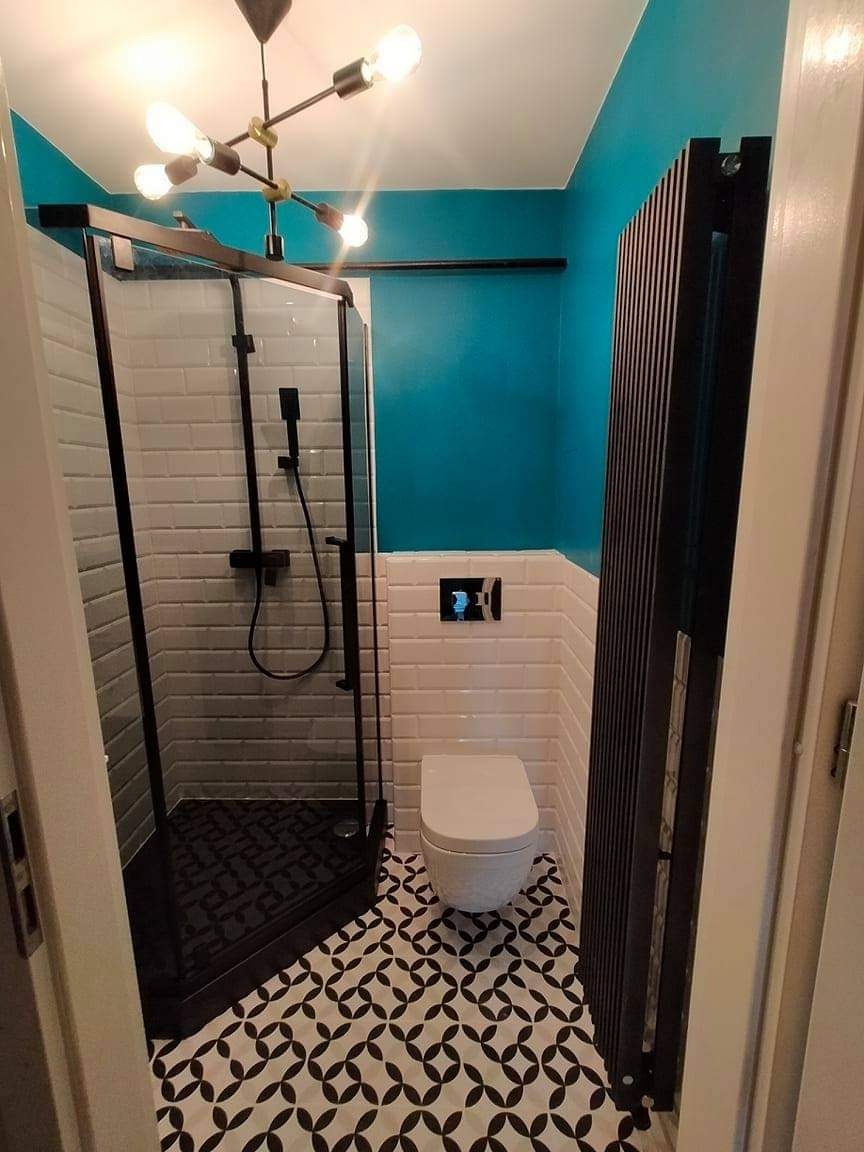 Wyremontowana łazienka w stylu nowoczesnym z kabiną prysznicową typu walk-in z czarnymi profilami, białą armaturą, wzorzystą czarno-białą podłogą i turkusową ścianą.