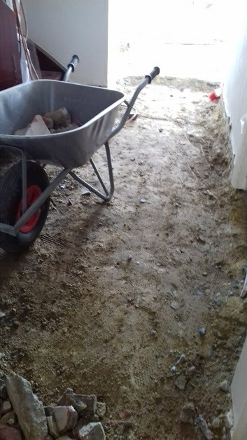 Przygotowanie podłoża pod wylewkę, widoczna taczka z gruzem i nierówna powierzchnia z odciśniętą siatką wzmacniającą.