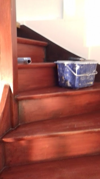 Malowane schody drewniane z niebieskim wiadrem i wałkiem malarskim na stopniu.