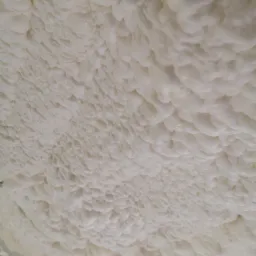 Pianka PUR o nieregularnej strukturze pokrywająca powierzchnię, widoczne nierówności i pęcherzyki powietrza w strukturze pianki.