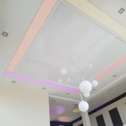 Nowoczesny sufit podwieszany z oświetleniem LED w kolorach różu, żółci i fioletu, uzupełniony o minimalistyczne, kuliste lampy wiszące.