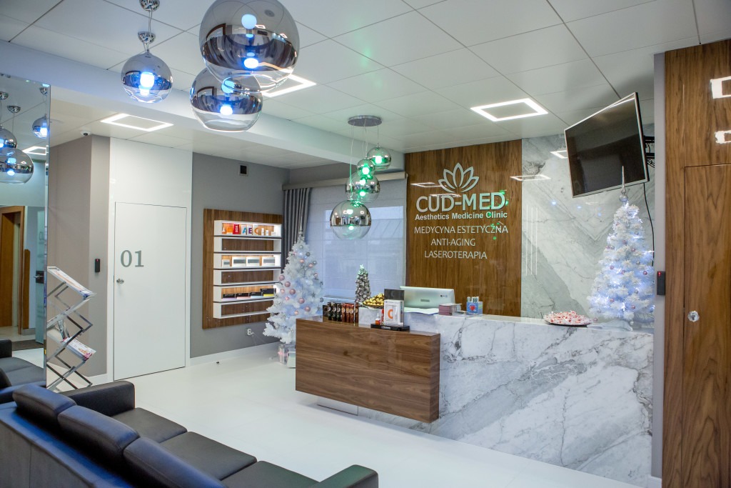 Nowoczesne wnętrze kliniki medycyny estetycznej z recepcją wykończoną marmurem, dekoracjami świątecznymi i designerskimi lampami wiszącymi.