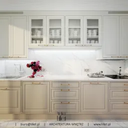 Elegancka kuchnia w odcieniach beżu i bieli, z marmurowym blatem i złotymi uchwytami, wyposażona w szklane szafki z białymi naczyniami i świeżymi czerwonymi różami w wazonie.