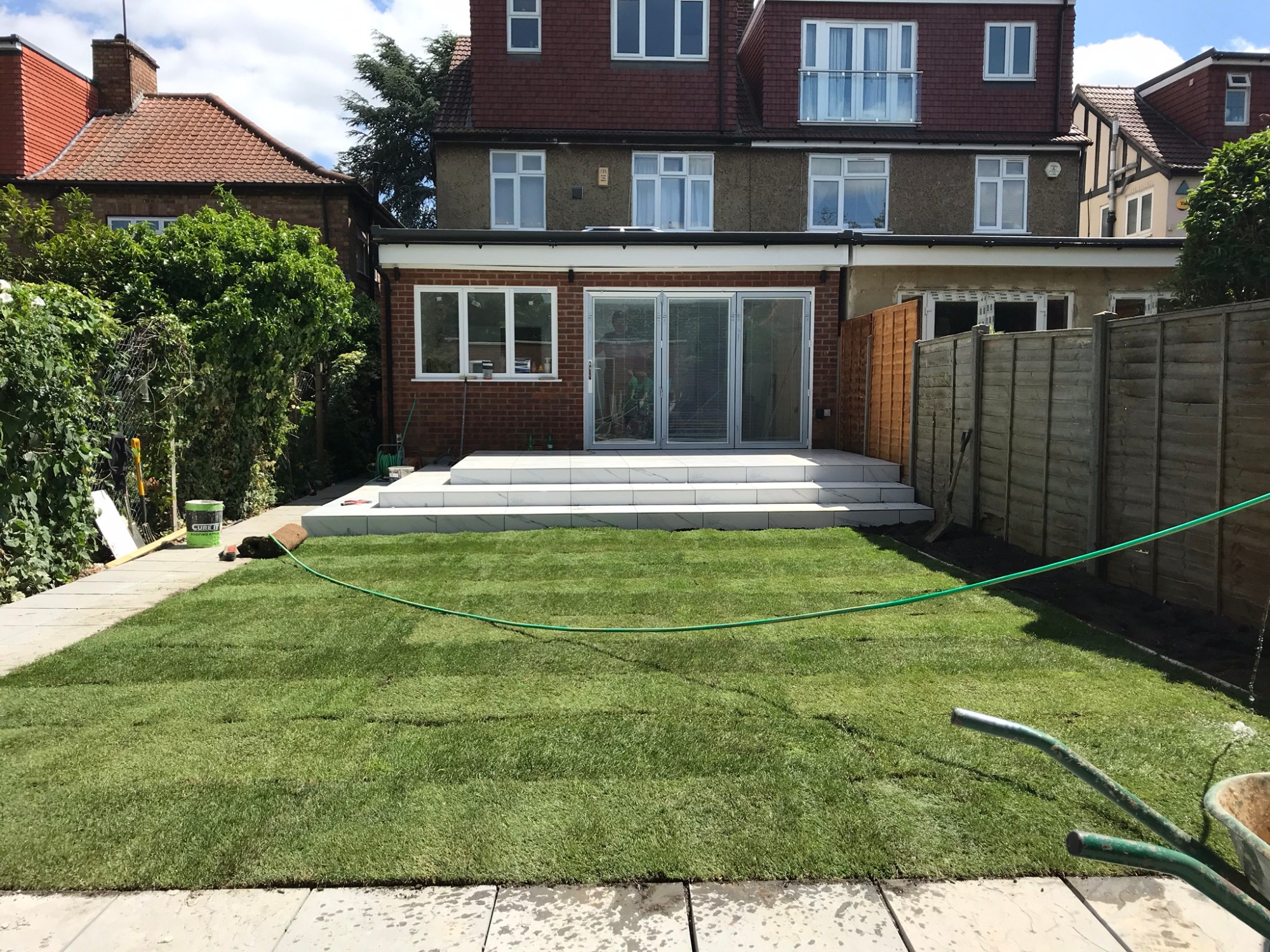 Nowo założony trawnik z rolki przed domem z przeszklonymi drzwiami tarasowymi i marmurowymi schodami.