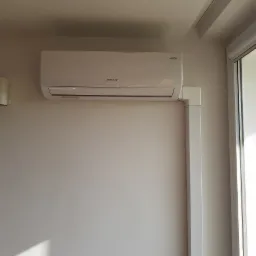 Biała jednostka wewnętrzna klimatyzacji Rotenso zamontowana na ścianie w pomieszczeniu z oknem, widoczne białe rury instalacyjne.