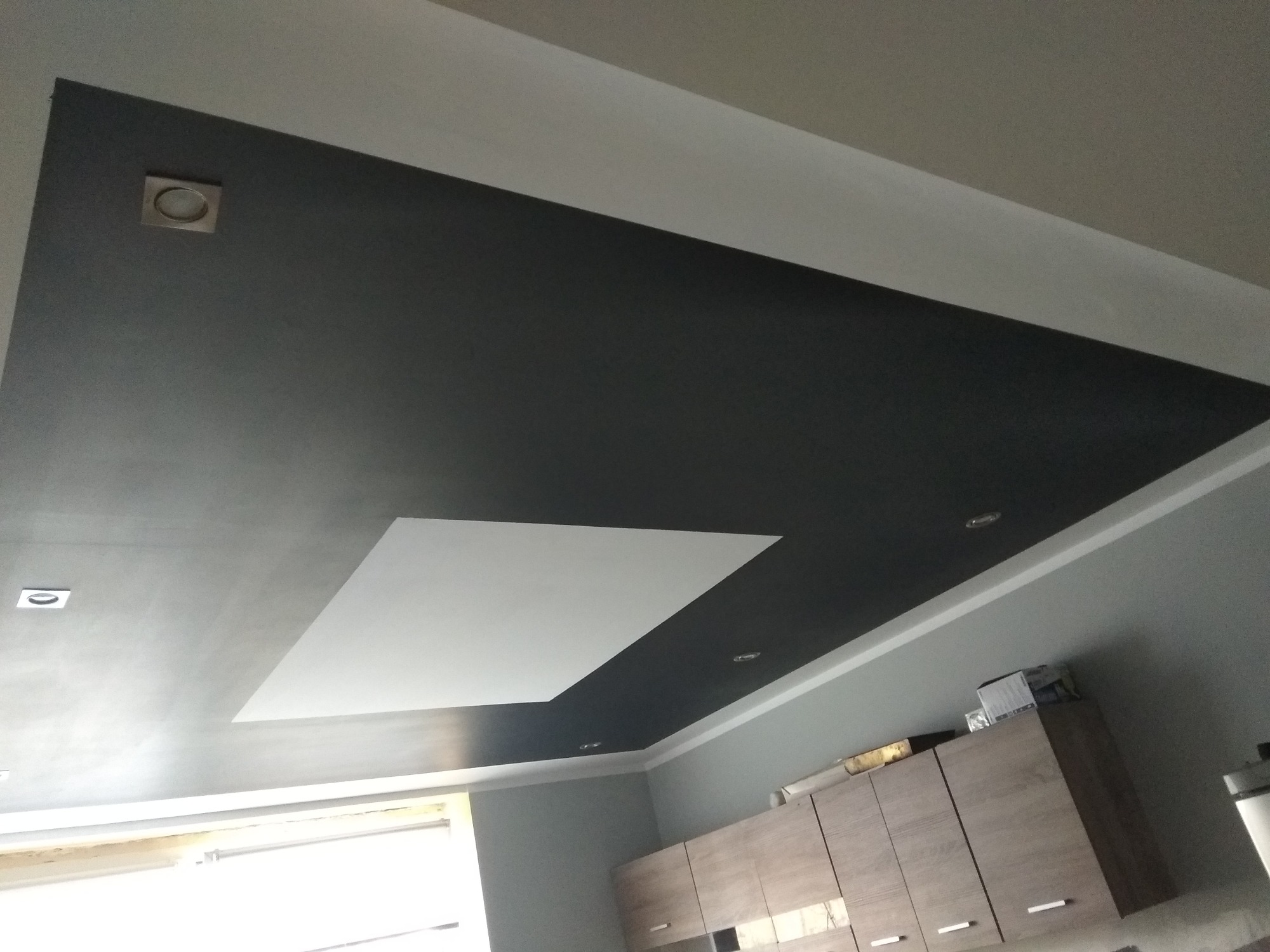 Dwukolorowy sufit podwieszany z wbudowanym oświetleniem punktowym, widok z dołu na tle szafek kuchennych.