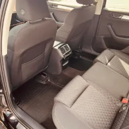 Wnętrze samochodu Skoda Superb z widocznymi tylnymi siedzeniami z pikowaną tapicerką, gumowe dywaniki pod nogami pasażerów z tyłu i kratka nawiewu klimatyzacji.