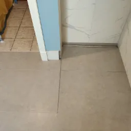 Ułożona podłoga z płytek w łazience z odpływem liniowym przy ścianie wykończonej marmurowymi płytami, widoczne narzędzia i pozostałości po remoncie.