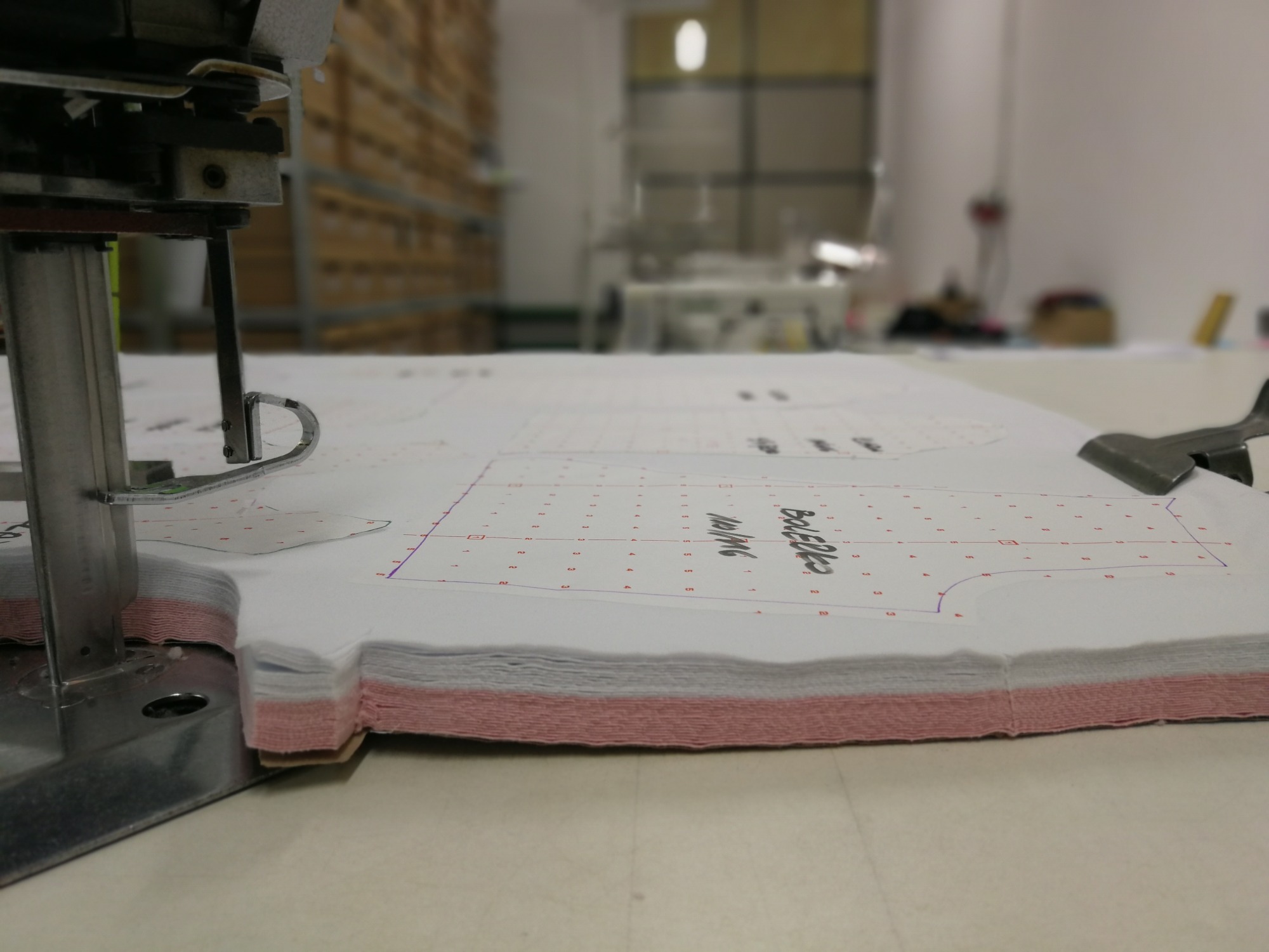 Wielowarstwowa tkanina z naniesionym szablonem kroju bolerka, przygotowana do cięcia maszynowego w pracowni krawieckiej.