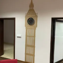 Beżowa dekoracja ścienna w kształcie Big Bena z wbudowanym zegarem, zamontowana na białej ścianie w biurze.