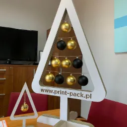 Kartnowe choinki z wyciętym laserowo logo firmy www.print-pack.pl, ozdobione złotymi i czarnymi bombkami, stoją na biurku w biurze.
