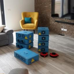 Ozon Piorun - Ozonowanie Gdańsk, Trójmiasto, Cała Polska - Niebieskie generatory ozonu ustawione w nowoczesnym salonie z szarą sofą, żółtym fotelem i ceglaną ścianą z telewizorem.