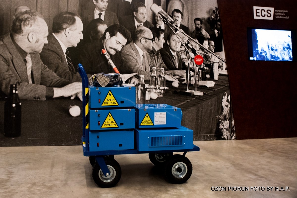 Wózek z urządzeniami do ozonowania firmy Ozon Piorun w Gdańsku, na tle zdjęcia z historycznego wydarzenia w ECS.