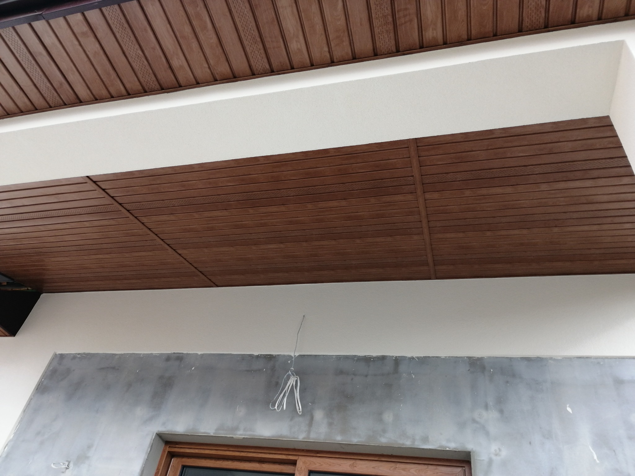 Montaż drewnopodobnej podbitki dachowej w Łomży, widoczne fragmenty elewacji w trakcie wykończenia i okno.