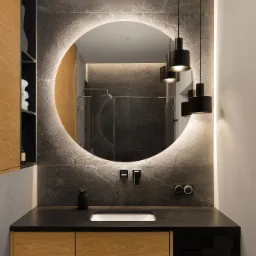 Nowoczesna łazienka w Pruszczu Gdańskim: okrągłe lustro z podświetleniem LED, czarny blat i drewniane szafki. Minimalistyczny design i eleganckie wykończenie.