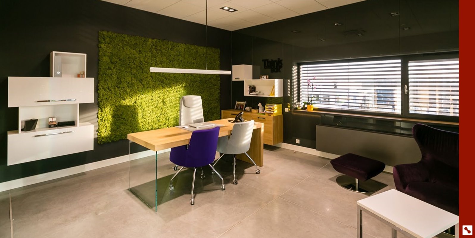 Nowoczesne biuro z drewnianym biurkiem na szklanych nogach, fioletowym i szarym krzesłem, ścianą z mchu, białymi szafkami wiszącymi i ciemnymi ścianami.
