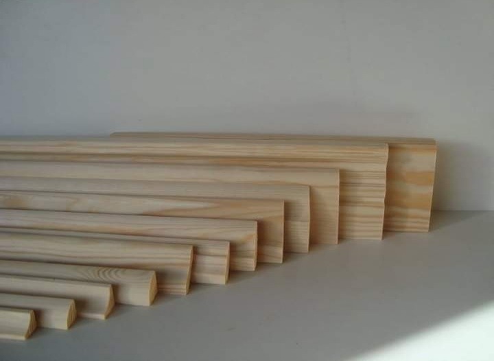Różne przekroje i długości listew przypodłogowych z jasnego drewna ułożone na białym tle.