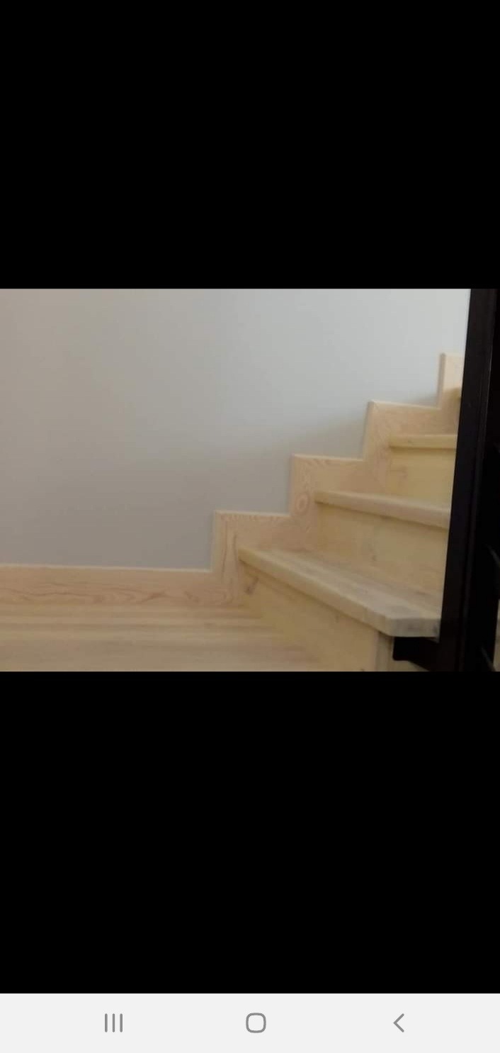 Jasne drewniane schody z czarną balustradą, widok z dołu, minimalistyczny design, szara ściana w tle.