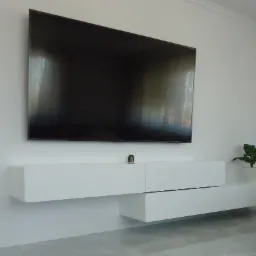 Minimalistyczna, biała szafka RTV pod telewizorem, z asymetrycznie wysuniętą szufladą, uzupełniona małą rośliną doniczkową i figurką.