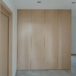 Świetlista, drewniana szafa wnękowa z czterema drzwiami, wkomponowana w ścianę, z subtelnym oświetleniem sufitowym i szarą podłogą, widziana pod kątem z lewej strony pokoju.