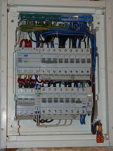 Otwarta skrzynka rozdzielcza z widocznymi bezpiecznikami, przewodami i listwami zaciskowymi wewnątrz białej obudowy.