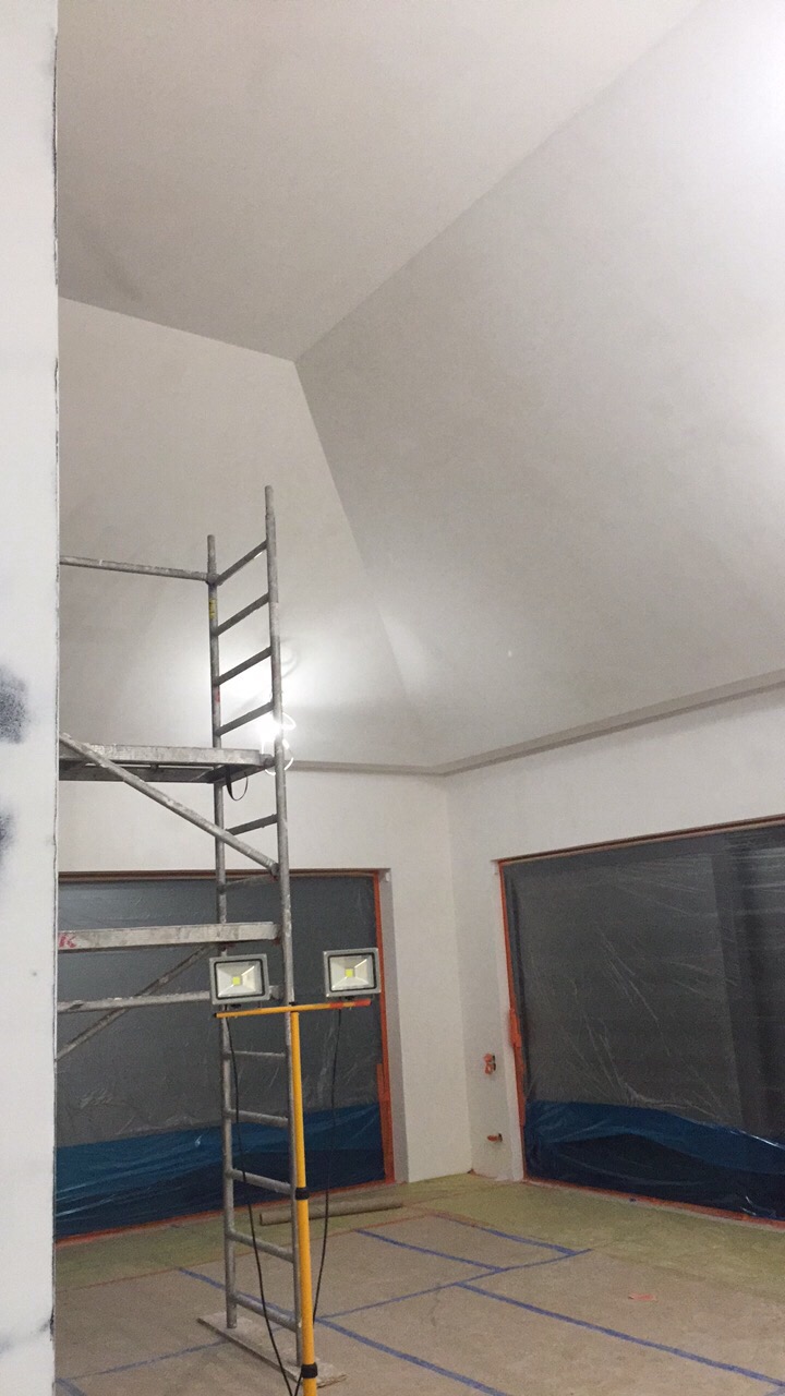 Wnętrze w trakcie remontu: sufit ze skosem po gładziowaniu, metalowe rusztowanie, okna zabezpieczone folią, podłoga z widocznymi śladami taśmy malarskiej.