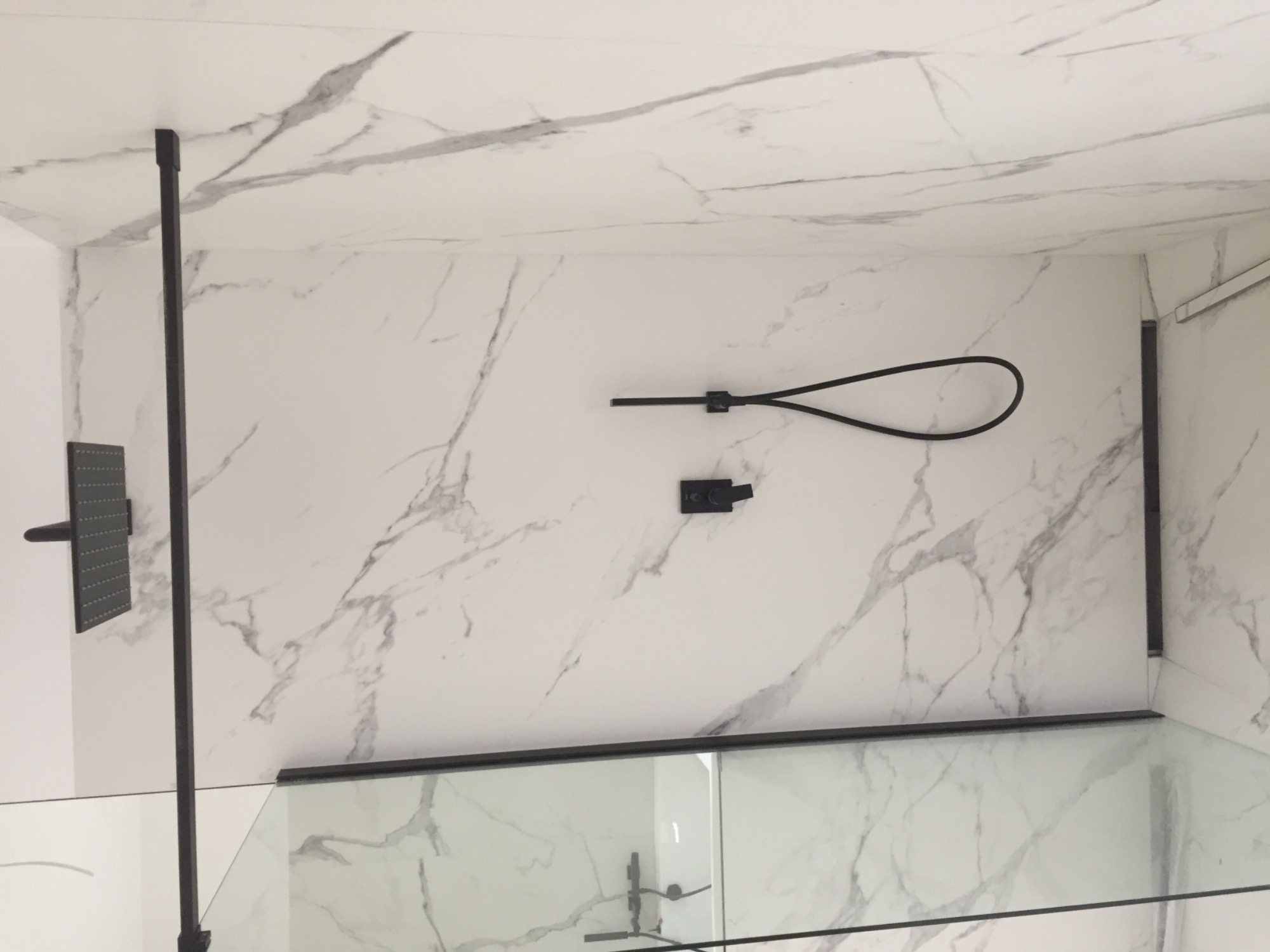 Nowoczesna kabina prysznicowa z czarną armaturą na tle białych płytek imitujących marmur.