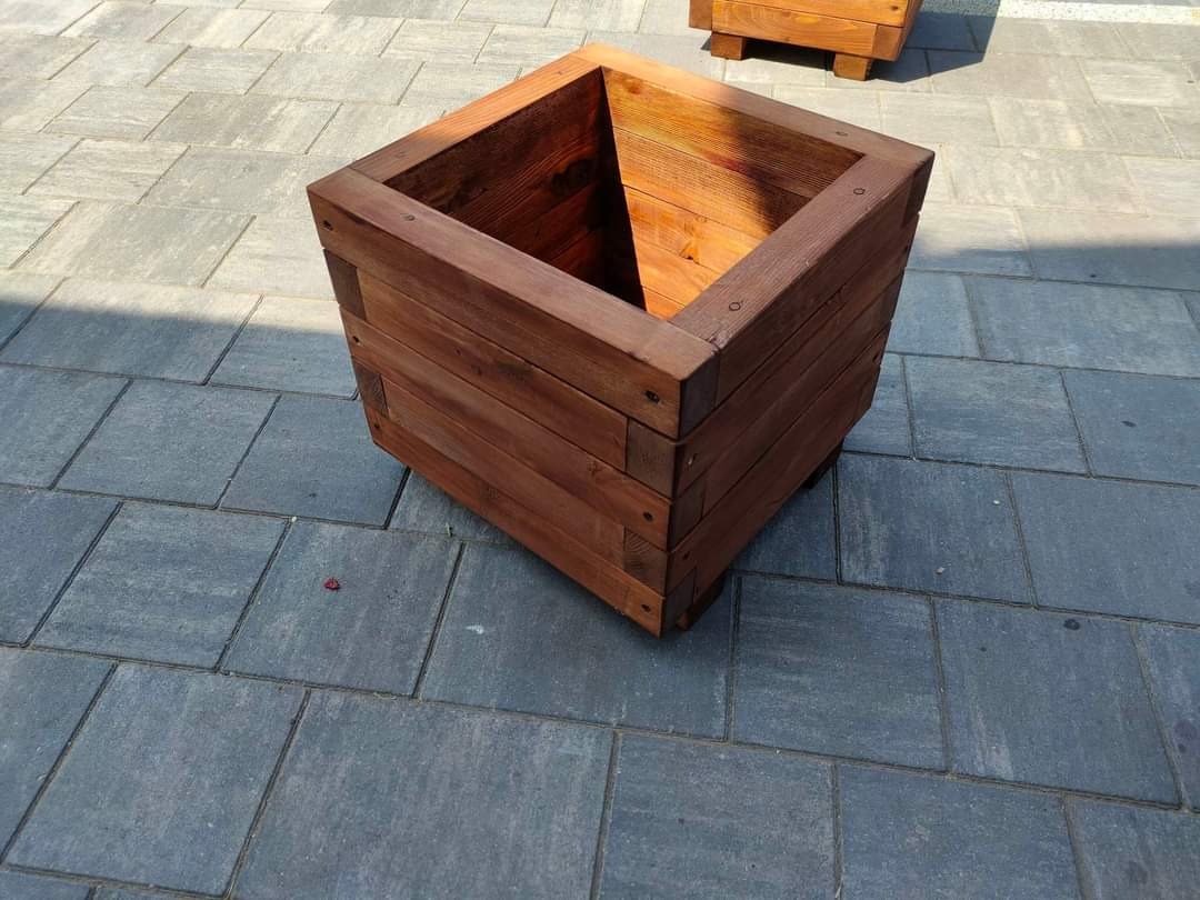 Kwadratowa, drewniana donica ogrodowa wykonana przez stolarza z Klonu, ustawiona na szarym bruku.